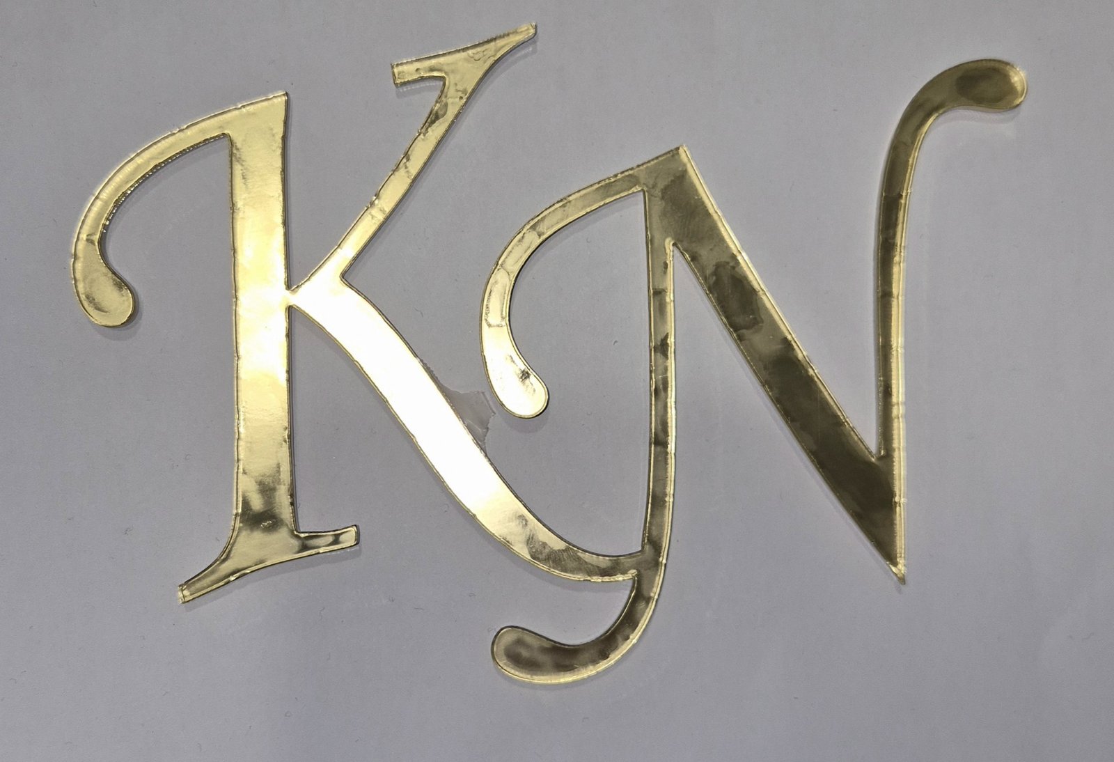 Μονογράμματα K και N κομμένα με laser σε χρυσό ακρυλικό καθρέφτη